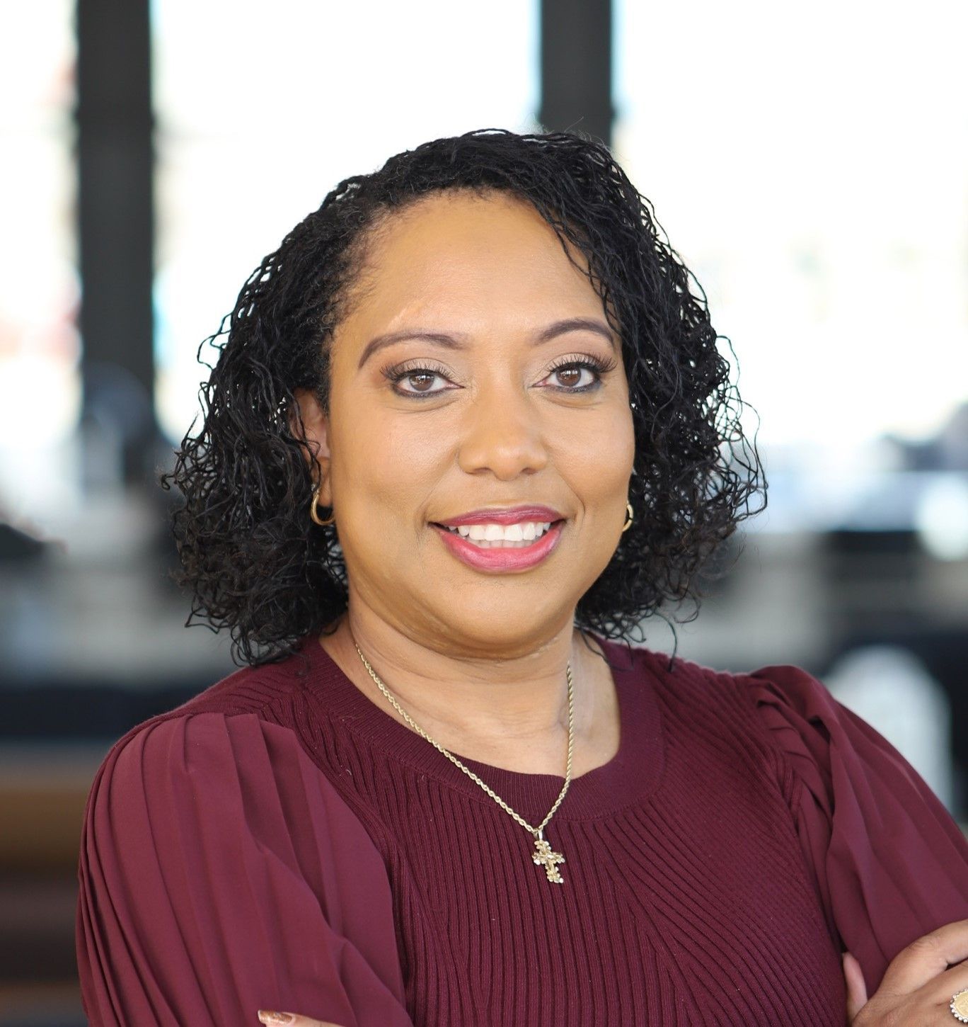 A woman wearing a maroon shirt and a necklace is smiling for the camera.