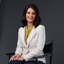 A woman is sitting in a chair wearing a white jacket and a yellow shirt.