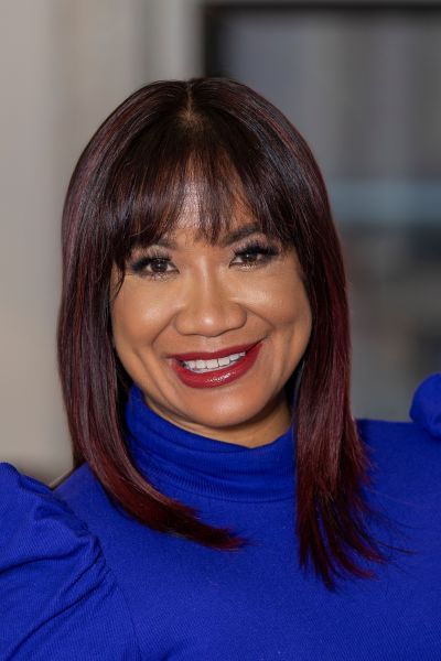 A woman wearing a black jacket and white earrings smiles for the camera