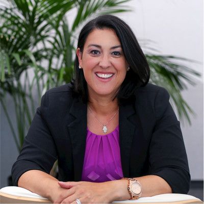 A woman wearing a purple shirt and a black jacket is smiling for the camera.