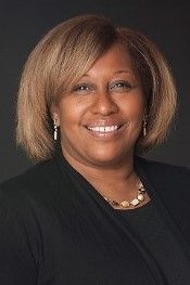 A woman wearing a black jacket and a necklace is smiling for the camera.