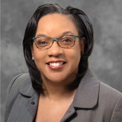 A woman wearing glasses and a grey jacket is smiling for the camera.