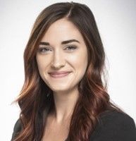 A woman with long brown hair is smiling and wearing a black jacket.