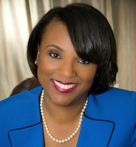 A woman wearing a blue jacket and pearl necklace smiles for the camera
