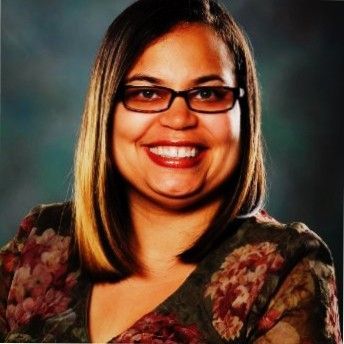 A woman wearing glasses and a floral shirt smiles for the camera
