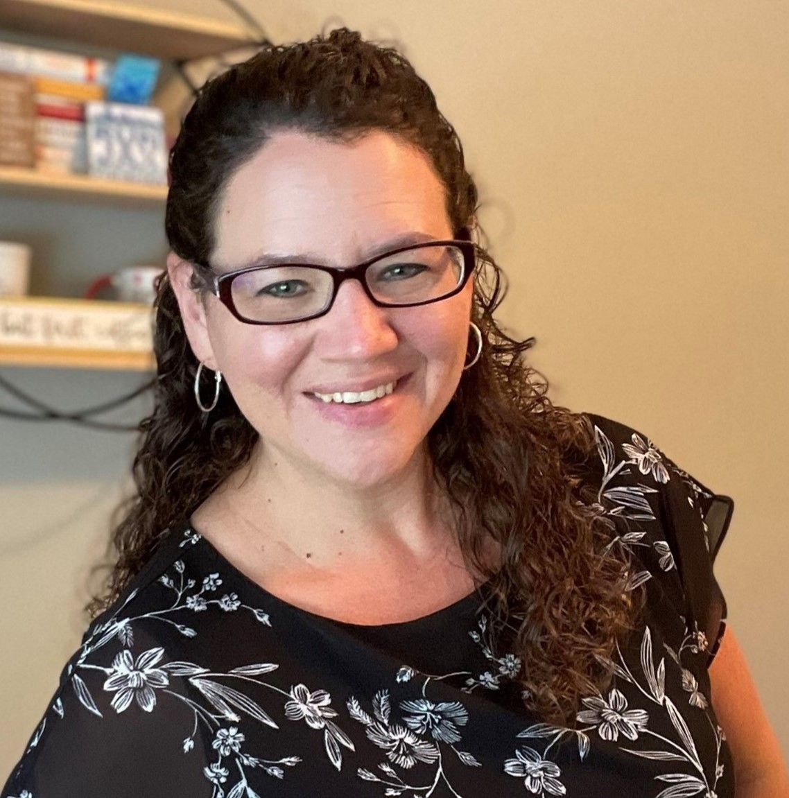 A woman wearing glasses and a floral shirt smiles for the camera