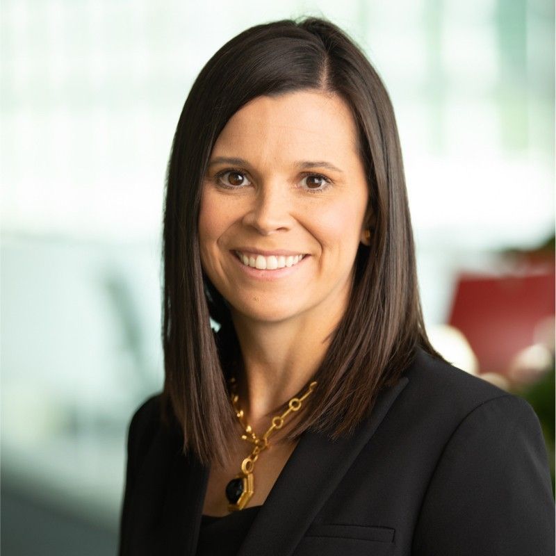 A woman wearing a black jacket and gold necklace smiles for the camera