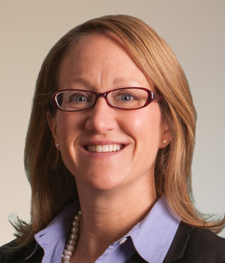 A woman wearing glasses and a pearl necklace smiles for the camera