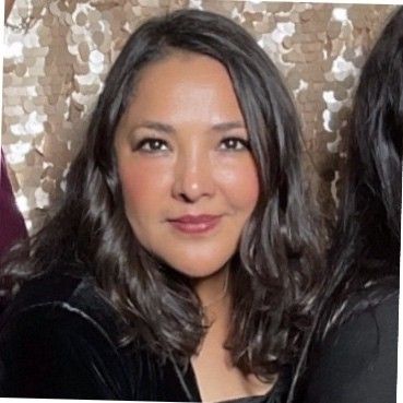 A woman with long dark hair is smiling in a photo booth.