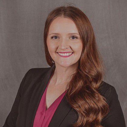 A woman with long red hair is wearing a black jacket and a pink shirt.