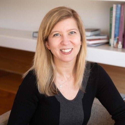A woman is smiling for the camera while sitting in front of a bookshelf.