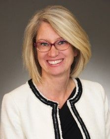A woman wearing glasses and a white jacket is smiling for the camera.