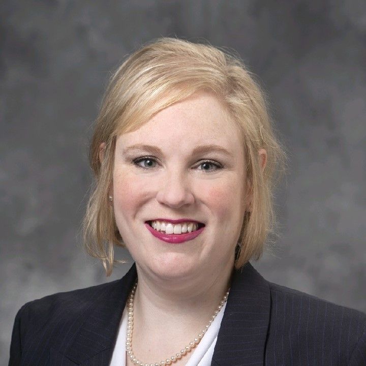 A woman in a suit and pearl necklace is smiling for the camera.