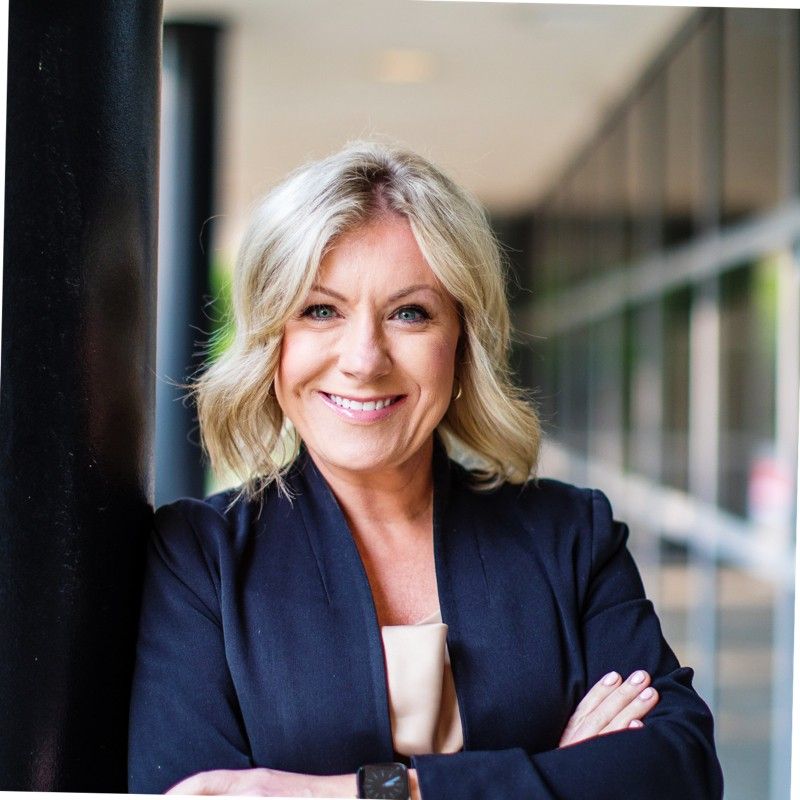 A woman in a black jacket is smiling with her arms crossed