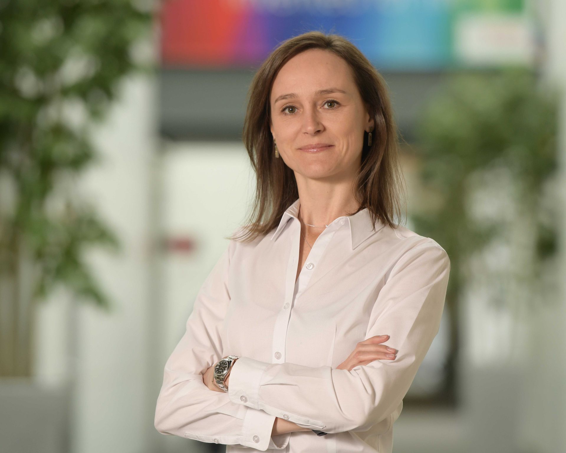 A woman in a white shirt is standing with her arms crossed in a hallway.