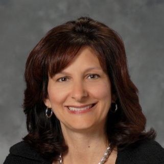 A woman wearing a blue jacket and necklace is smiling for the camera.