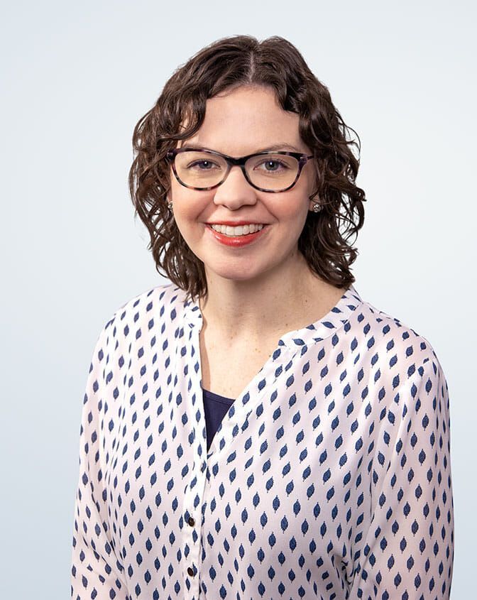 A woman wearing glasses and a blue jacket is smiling for the camera.