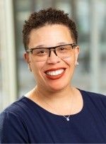 A woman wearing glasses and a blue shirt is smiling for the camera.