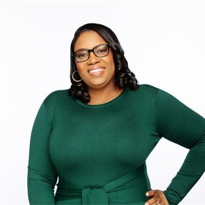 A woman wearing glasses and a green dress is smiling for the camera.