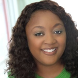 A woman with curly hair is wearing a green sweater and smiling.