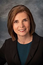 A woman in a black jacket and blue shirt is smiling for the camera.