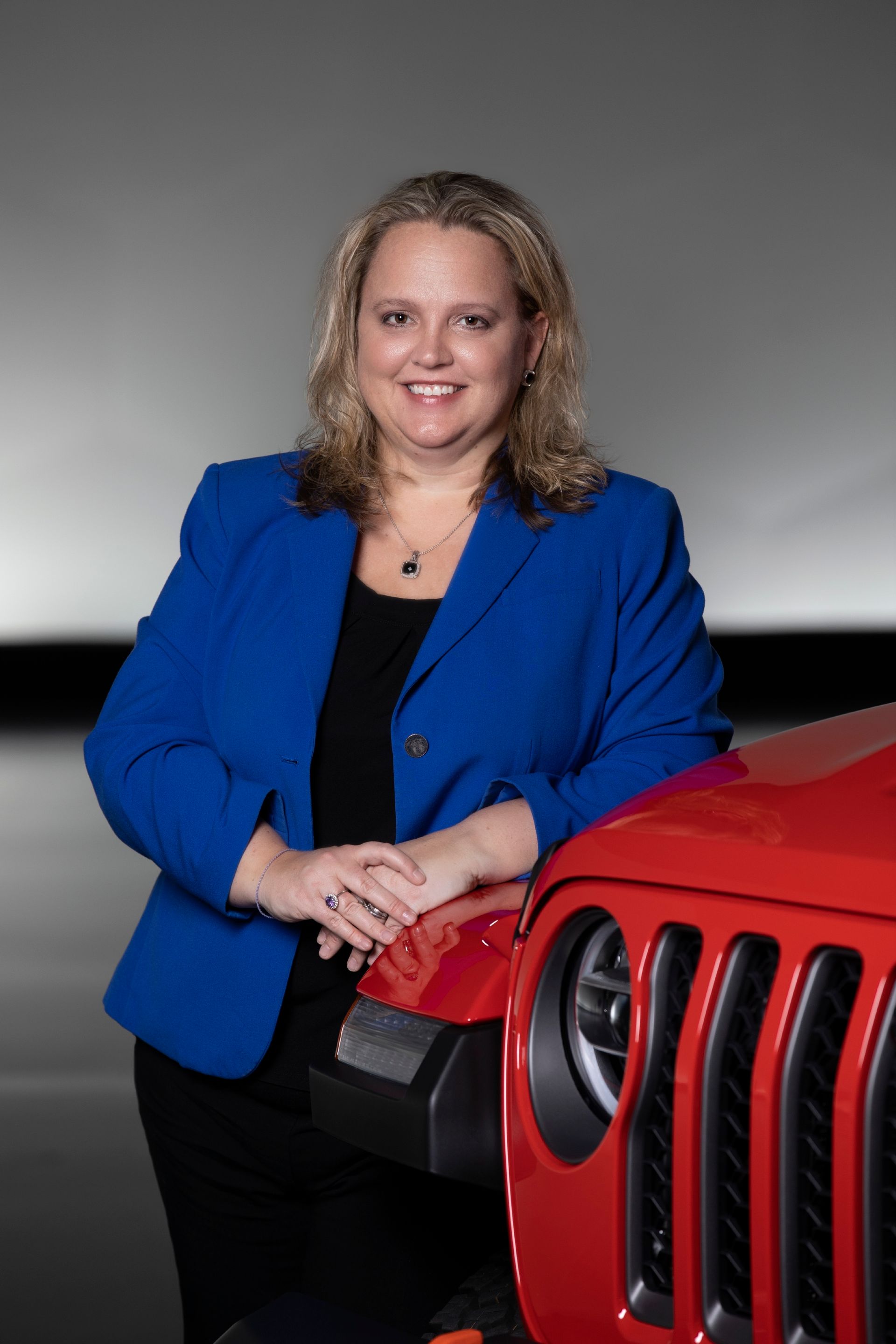 A woman in a blue jacket is standing next to a red jeep.
