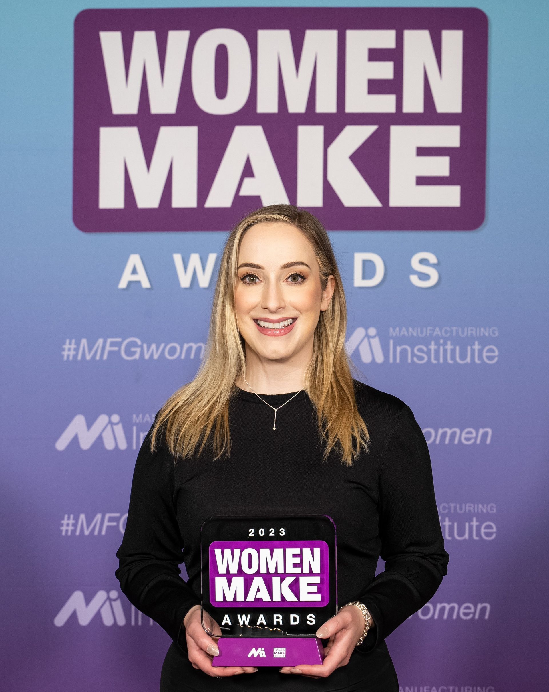 A woman is holding an award in front of a sign that says women make awards