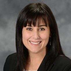 A woman in a black jacket and white shirt is smiling for the camera.