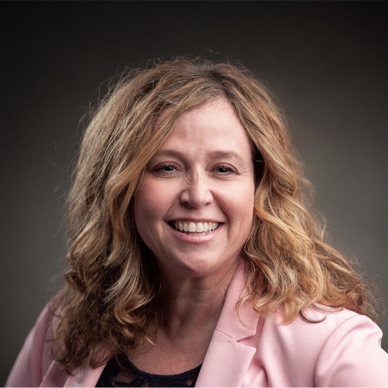 A woman in a pink jacket is smiling for the camera.