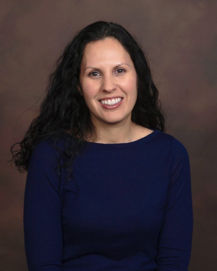 A woman in a blue shirt is smiling for the camera.