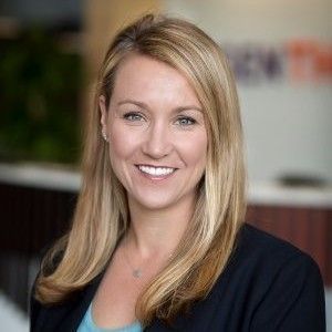A woman in a black jacket and blue shirt is smiling for the camera.