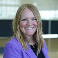 A woman wearing a black jacket and gold necklace smiles for the camera