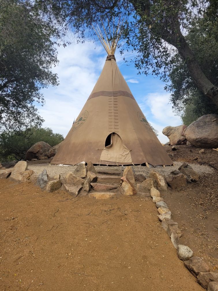 A teepee is sitting on top of a dirt hill surrounded by rocks and trees.