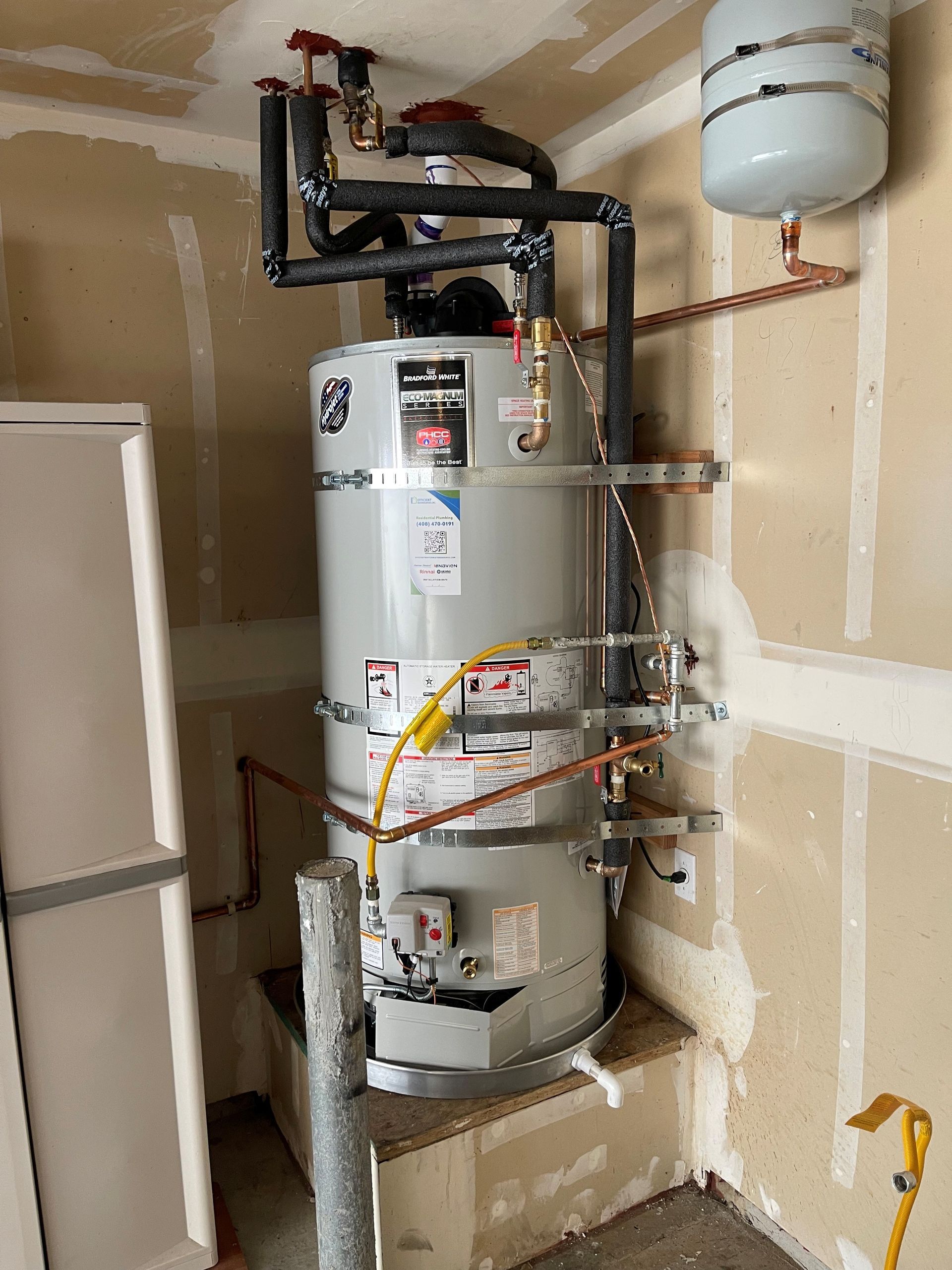 Water heater with pipes and expansion tank in an unfinished utility closet.