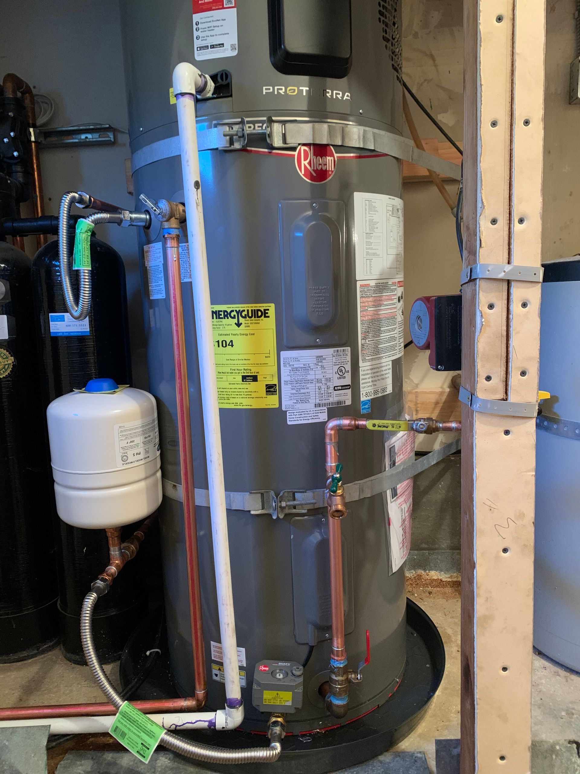 Water heater in a utility closet with pipes, a small expansion tank, and a black drain pan.