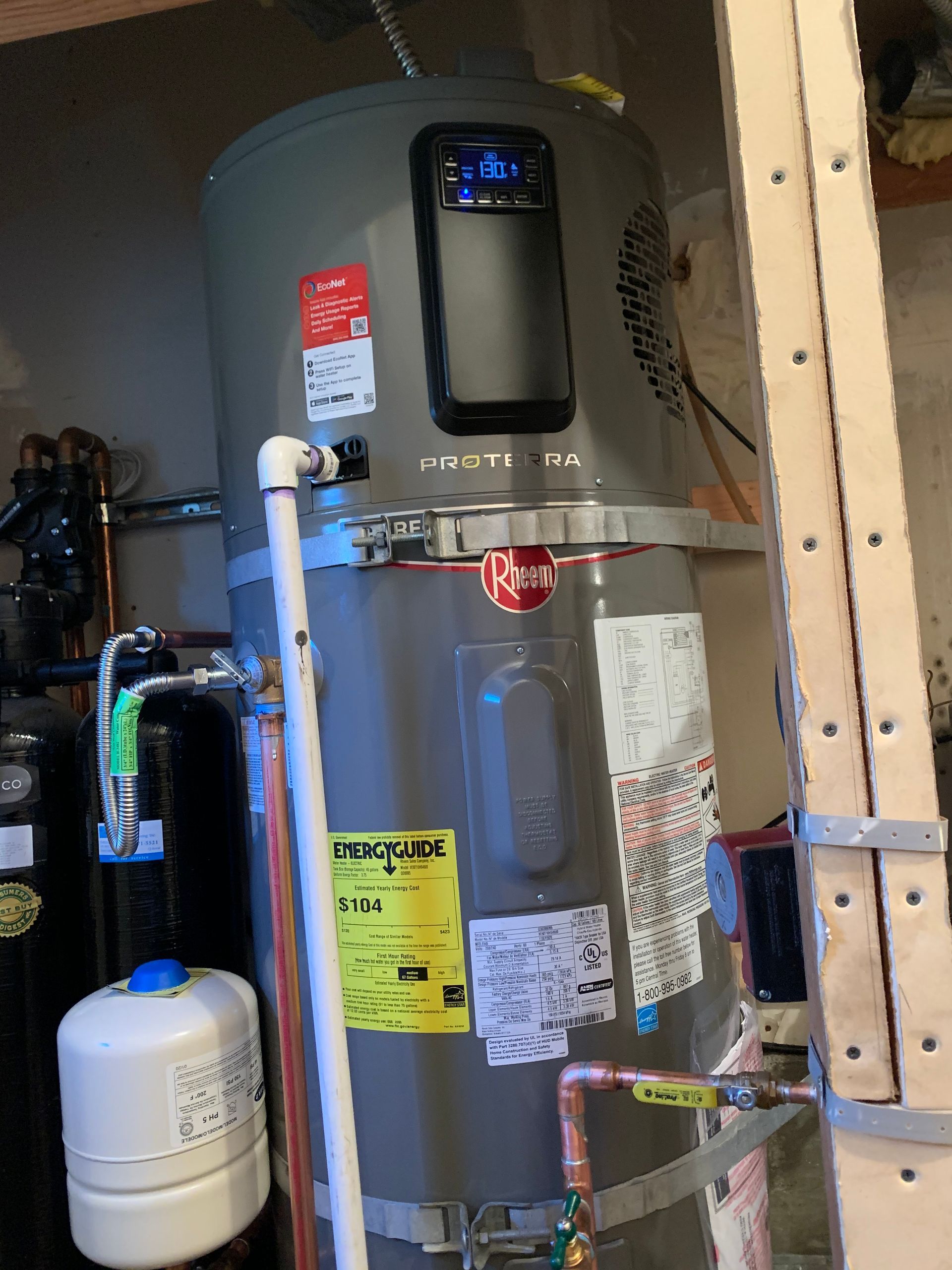 Gray water heater with pipes, pressure tank, and labels in a utility closet.