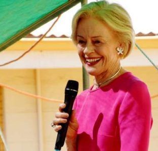 A woman in a pink shirt is holding a microphone and smiling