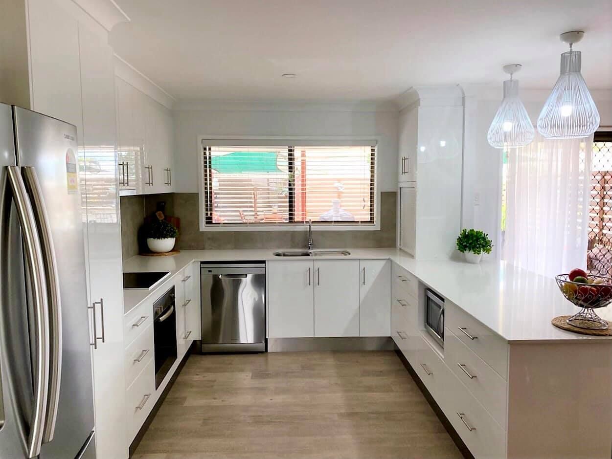 Modern white kitchen with stainless steel appliances, a long countertop, and window.