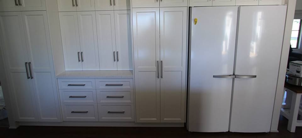 White kitchen cabinets and refrigerator. Dark hardware, drawers, and tall built-ins.