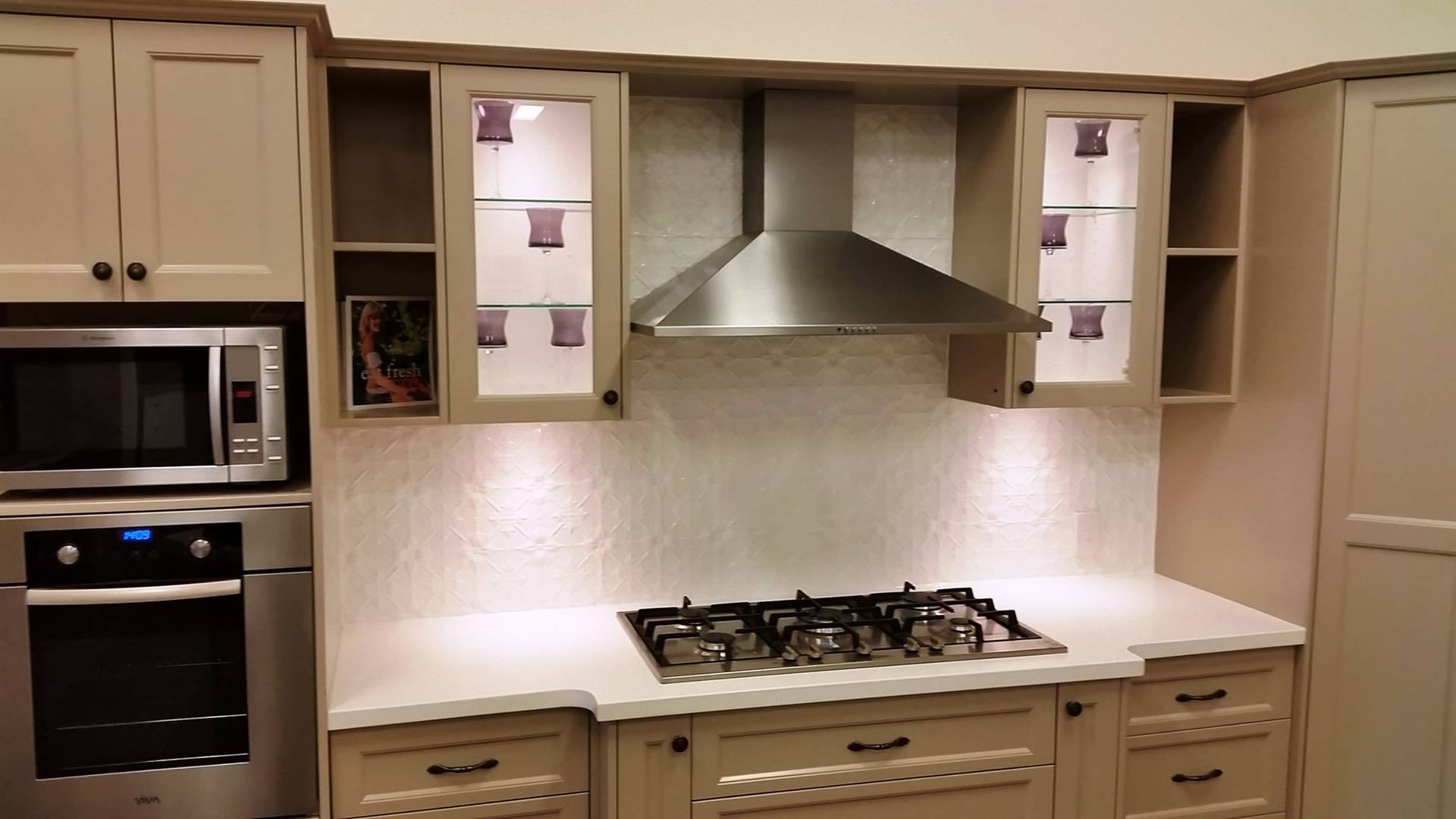 Kitchen with light-colored cabinets, stainless steel appliances, cooktop, and range hood.
