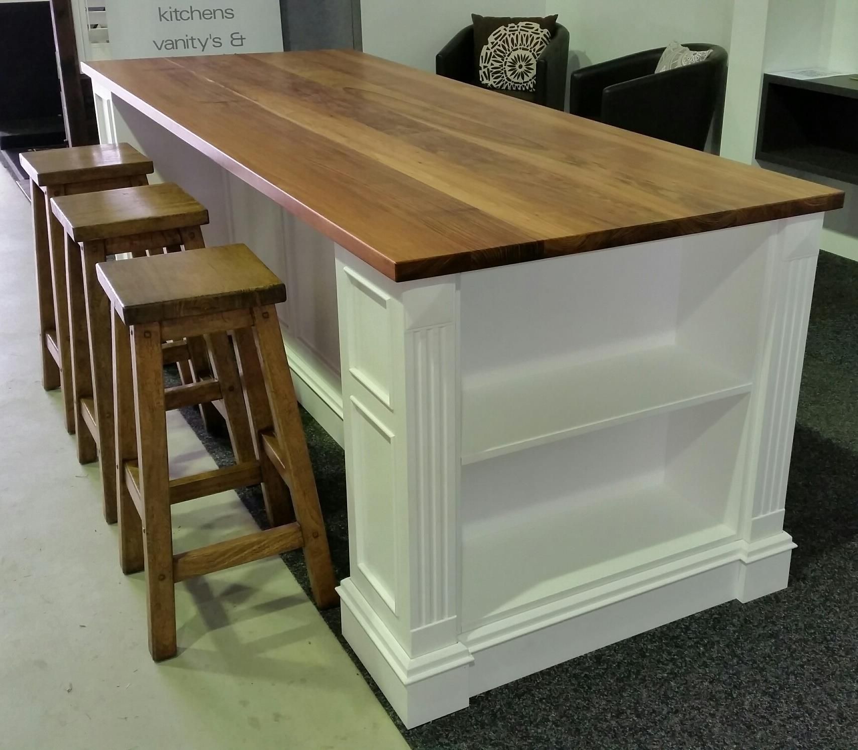 Wooden kitchen island with shelves and four stools. White base, wood countertop.