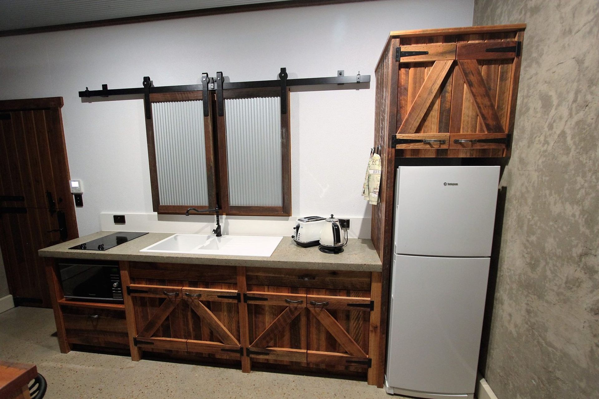 Rustic kitchen with wooden cabinets, a sink, and a refrigerator. A window with sliding doors is above the sink.