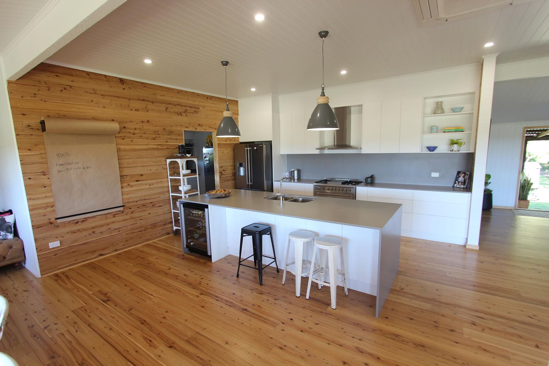 Kitchen with wood accent wall, white cabinetry, island with stools, and pendant lights.