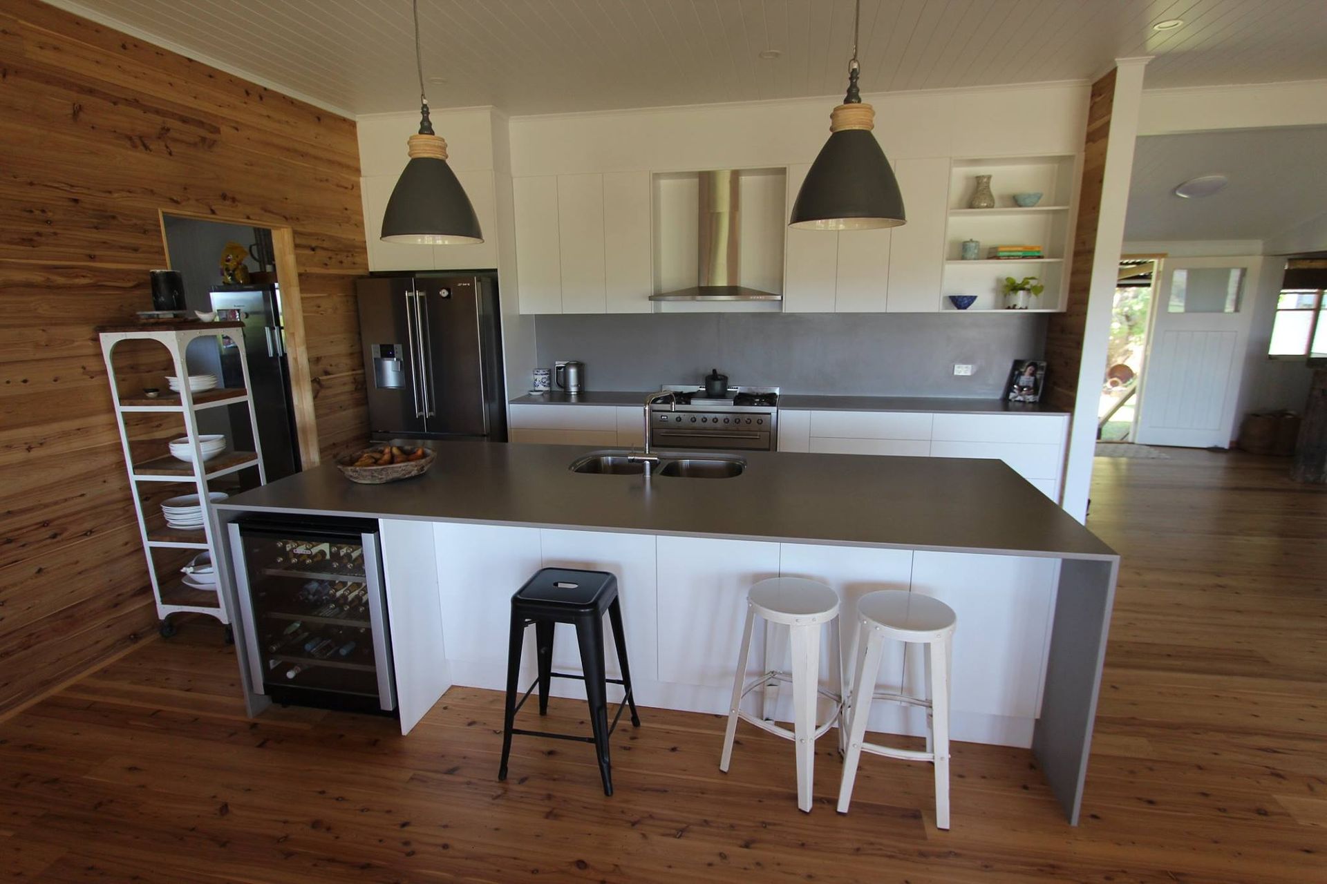 Modern kitchen with white cabinets, gray countertops, wooden floors, and a wine fridge.