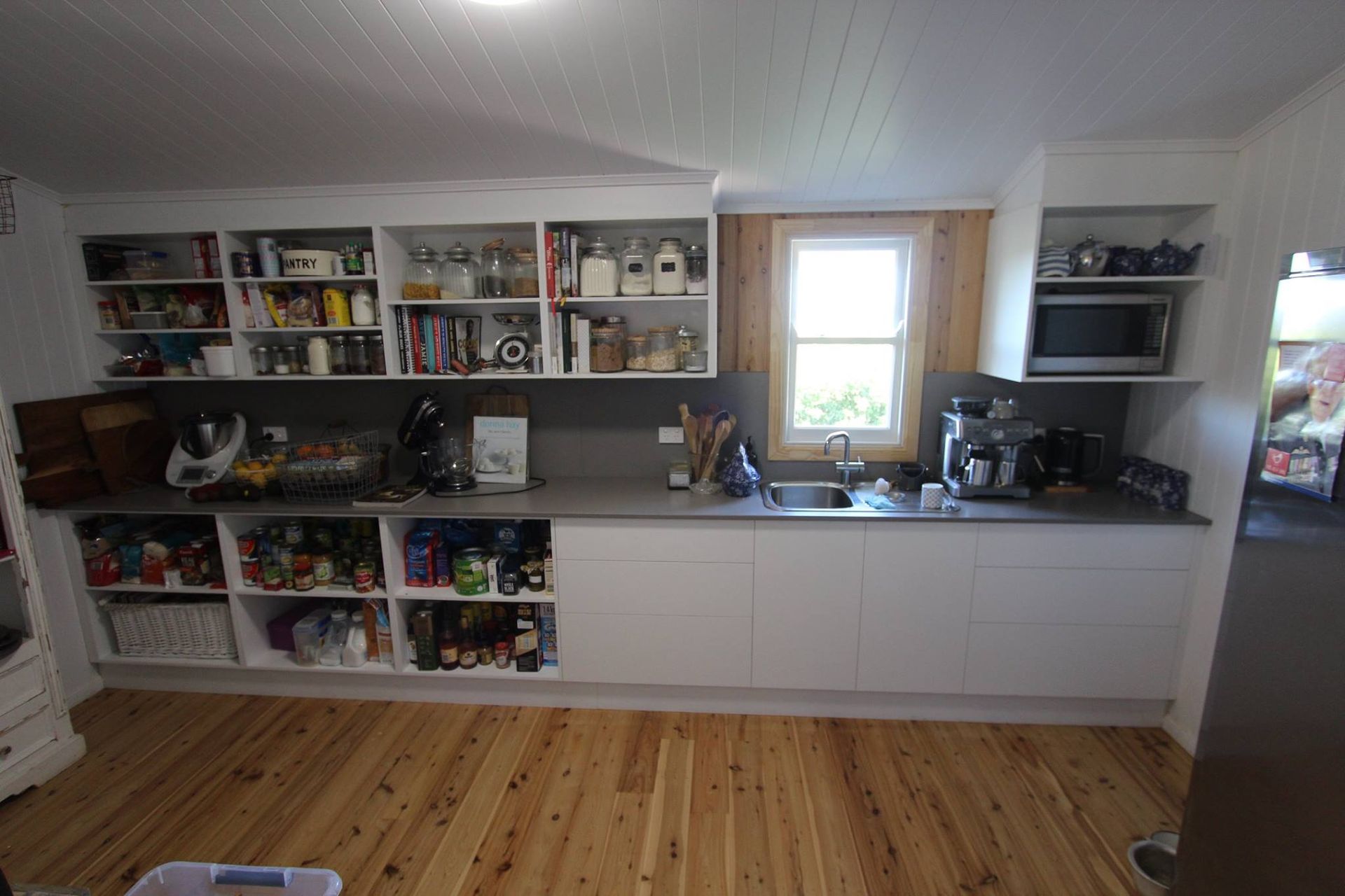 Kitchen with white cabinets, countertop, window, shelves with items, and wooden floor.