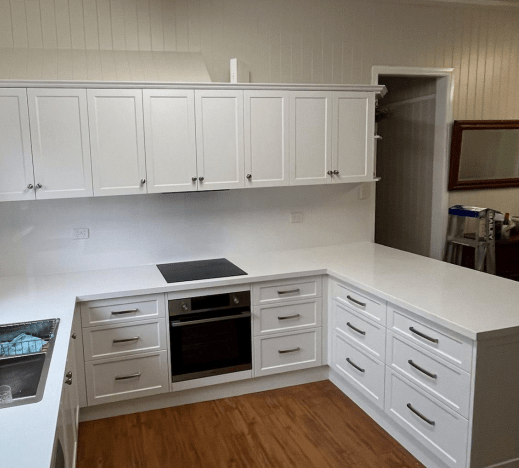 White kitchen with quartz countertops and cabinets, built-in oven and cooktop, and wood floor.