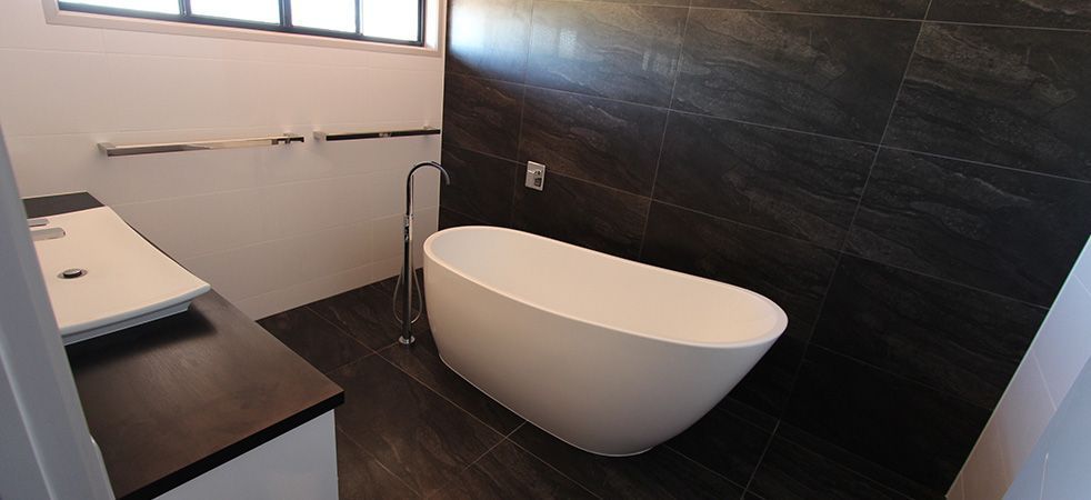 Modern bathroom with a white freestanding bathtub and dark tile walls and floor.