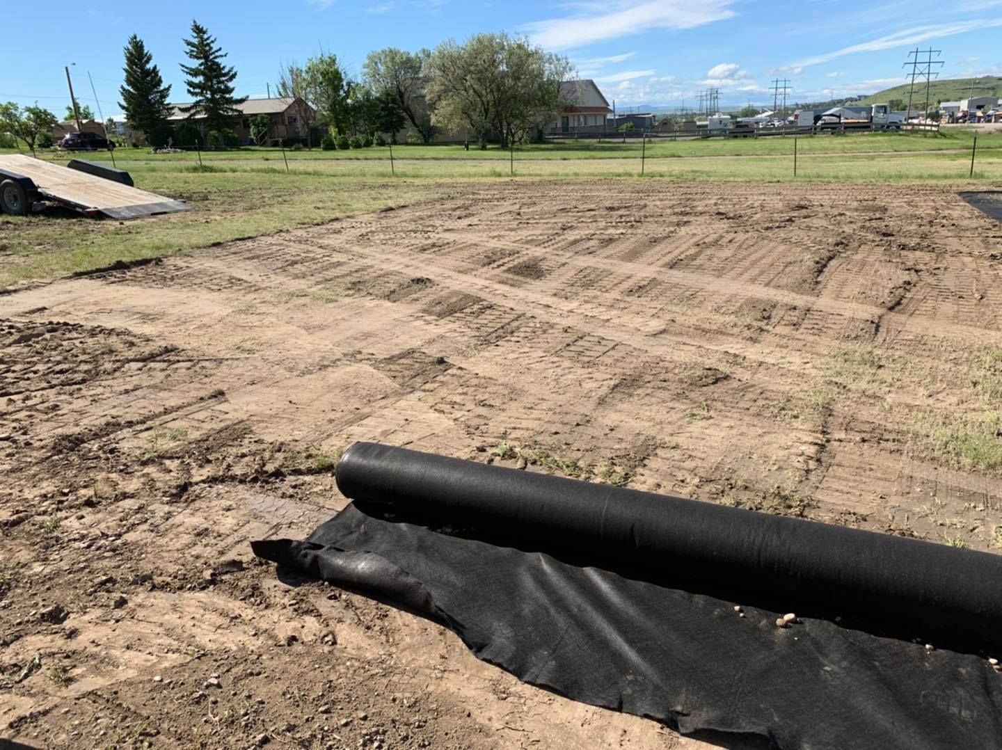 An excavator works on a desert construction site, grading soil near an area lined with heavy-duty plastic sheeting.