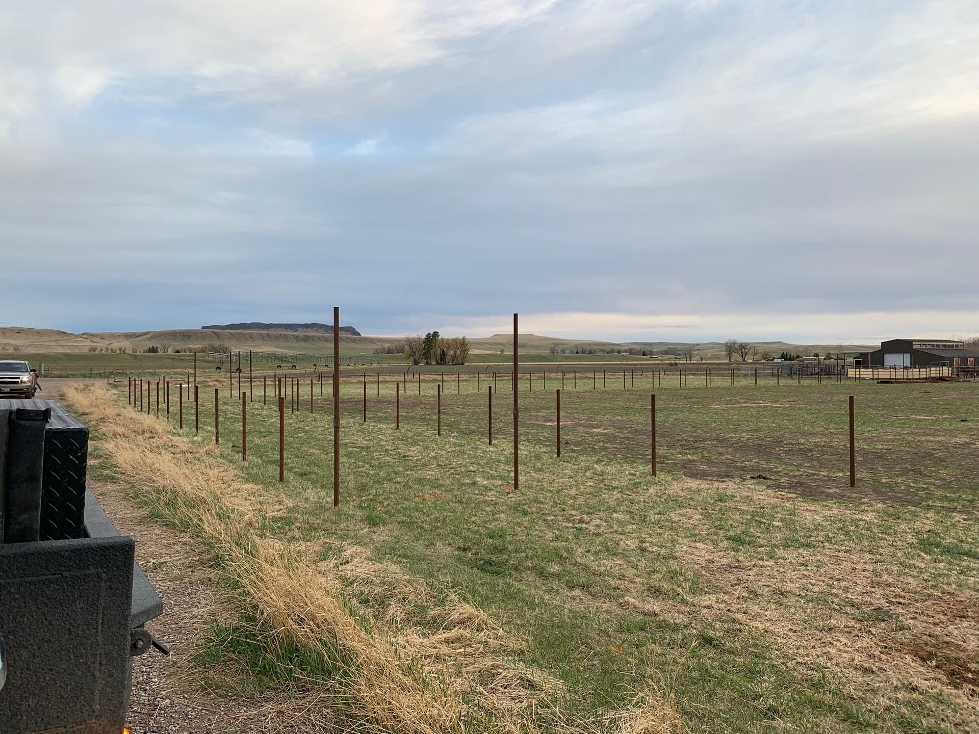 A line of metal fence posts stands in a rural field under a cloudy, overcast sky.