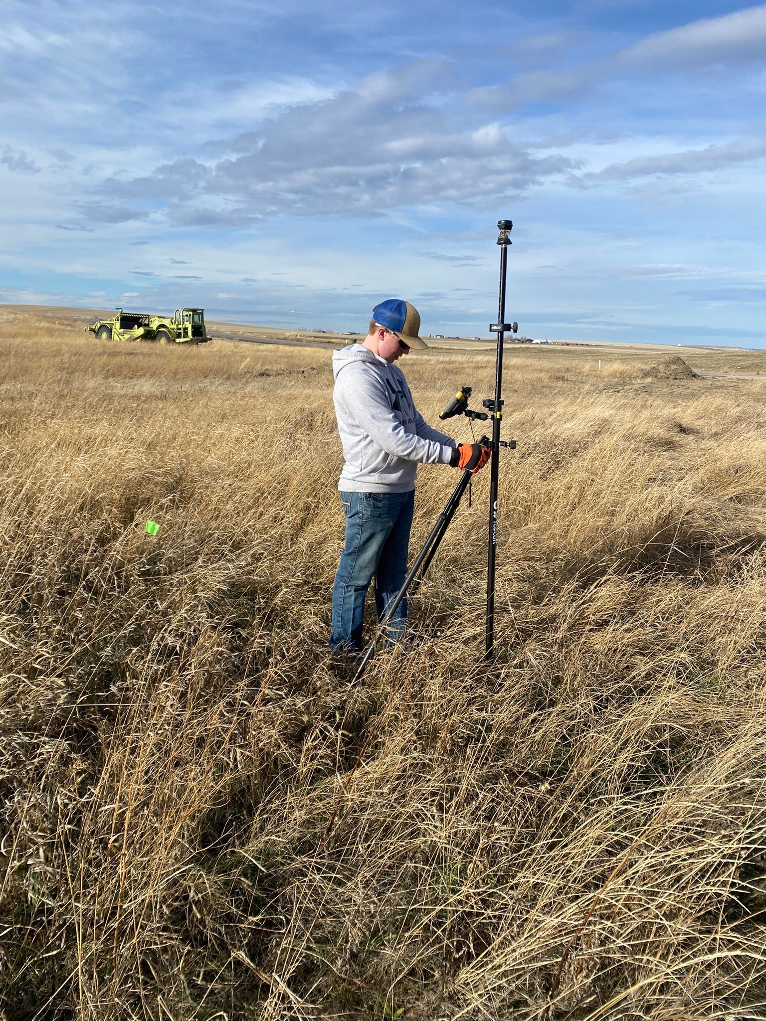 A person uses a hose to empty water from an above-ground pool into a muddy trench outdoors.